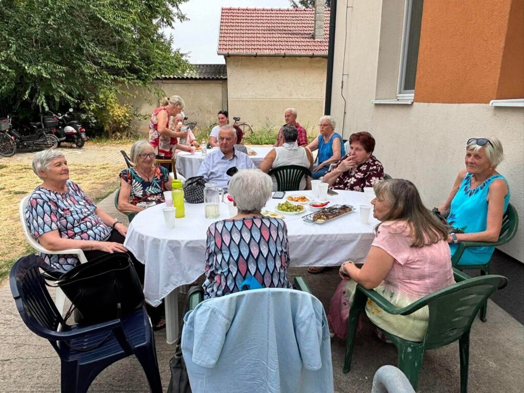 A baráti társaság beszélget egy kertben, asztalnál.