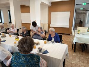 Születésnapok megünneplése az Idősek otthonában egy terített asztal mellett több idős.