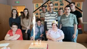 Szülinapi köszöntő, tortával, gyertyával, sziporkával, háttérben a társak.